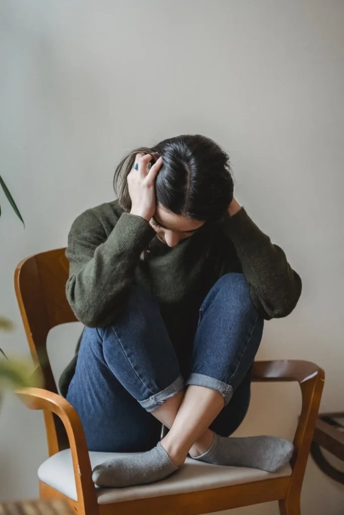 stressed woman sitting cross-legged in a chair with her head in her hands