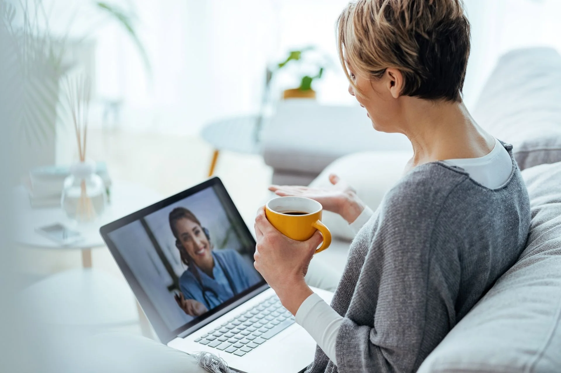 woman drinking coffee on her couch while on a video call